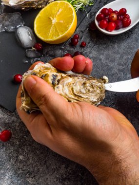 Bıçaklı bir adam taze bir istiridye açar. Limonlu, buzlu, dutlu, seçici odaklı koyu taş arka plan.