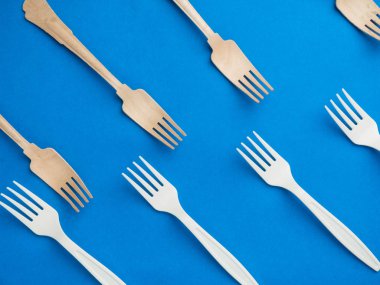 Organik bambu kullan-at çatallar plastiklere karşı moda mavi arka planda. Çevre dostu ahşap ve küfürsüz plastik çatallar.
