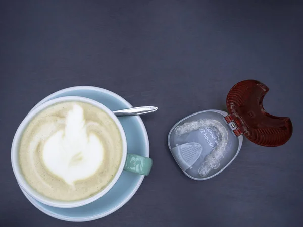 Δόντια aligners σε κουτί, κεραμικό φλιτζάνι τέχνης latte σε ένα καφέ καπουτσίνο σε μπλε κύπελλο στο μοντέρνο 2020 χρώμα — Φωτογραφία Αρχείου