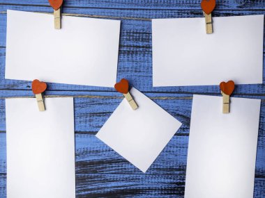 A white square sheet of paper is attached by red wooden pins in the form of hearts on trendy blue background Blank for Valentine's day,wedding,love message