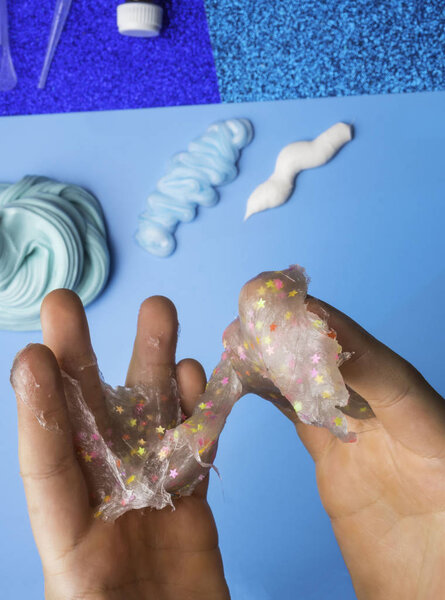 Компоненты для приготовления самодельной слизи. Светящаяся слизь с красочными декоративными звездами в детских руках. Вид сверху. Образование и хобби
