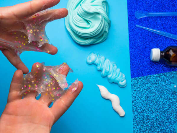 Компоненты для приготовления самодельной слизи. Светящаяся слизь с красочными декоративными звездами в детских руках. Вид сверху. Образование и хобби
