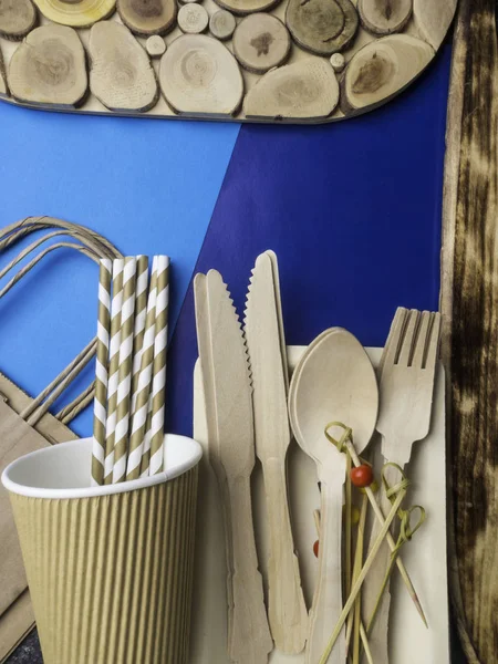 Disposable wooden cutlery and paper bag on trendy blue color background, cutlery, recycling and eco friendly concept, plastic-free alternatives zero waste environmental protection