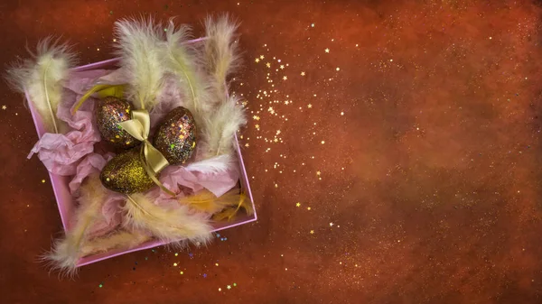 Huevos de Pascua en una caja de regalo rosa con plumas, decoración de Pascua. Nido con huevos rojos dorados sobre fondo rojo festivo con purpurina. Tarjeta de felicitación. Feliz Pascua . — Foto de Stock