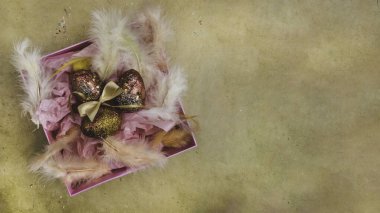 Paskalya yumurtaları pembe hediye kutusunda, tüylü, paskalya süslemeli. Kutlama kartında altın sarısı yumurtaları olan bir yuva. Mutlu Paskalyalar.