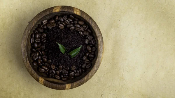 Kosmetyki domowej roboty z peelingiem do kawy, fasolą i zielonymi liśćmi na drewnianej misce na żółtym ekologicznym tle — Zdjęcie stockowe
