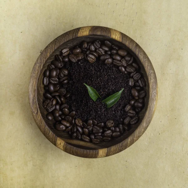 Hemgjorda kosmetika med kaffe skrubba på träskål på gul miljövänlig bakgrund, gröna blomblad. Närbild — Stockfoto