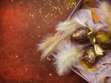 Paskalya yumurtaları pembe hediye kutusunda, tüylü, paskalya süslemeli. Kırmızı arka planda altın kırmızı yumurtalı, ışıltılı bir yuva. Tebrik kartı. Mutlu Paskalyalar. Seçici odak