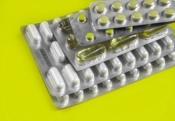 Capsules and pills packed in blisters on yellow background. Tablets. Medicine symbol. Medications drugs