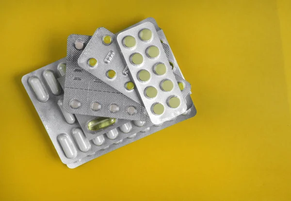 Capsules and pills packed in blisters on yellow background. Tablets. Medicine symbol. Medications drugs, flat lay, overhead
