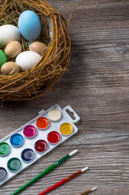 Yuvada paskalya yumurtaları ve ahşap arka planda renkli boya ve fırçalar. Resim yapmaya başlıyorum. Kapat.