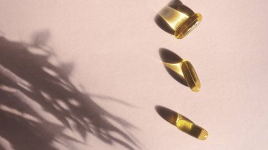 Çiçek gölgesi, vitamin ve antioksidan konsepti Omega 3, karaciğer morina ya da akşam primoz yağı içeren pembe arka planda yağlı jelatin kapsüller. Minimalizm. Boşluğu kopyala.
