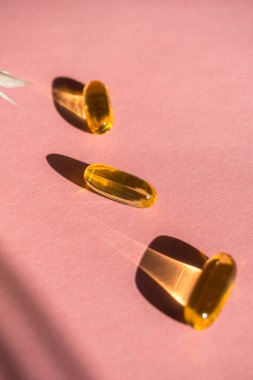 Pembe arka planda yağlı sarı kapsüller, vitaminler ve antioksidan konsepti Omega 3, sağlık hizmetleri için karaciğer morina ya da primoz yağı. Moda gölgesi, seçici odak