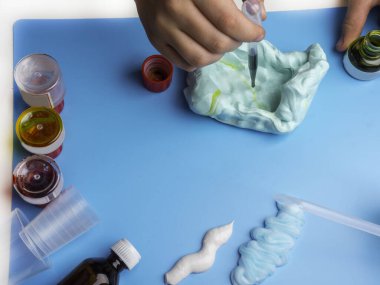 Sümük yapmak için bileşenler. Çocuk eğitimi konsepti. Diş macunu, tıraş köpüğü, dekoratif aksesuarlar, mavi arka planda boya, çocuk eli sanat aktivitesi.