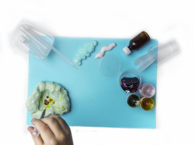 Sümük yapmak için bileşenler. Çocuk eğitimi konsepti. Diş macunu, tıraş köpüğü, dekoratif aksesuarlar, mavi arka planda boya, çocuk eli sanat aktivitesi.