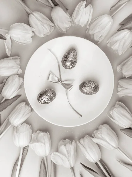 monochrome composition for Easter with tulip and white plate with painted eggs. Top view. Happy easter concept