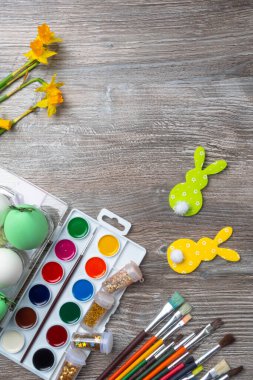 Paskalya yumurtaları, renkli boya ve fırçalar, sarı çiçekler narsist, ahşap arka planda tavşan. Resim yapmaya başlıyorum. Boşluğu kopyala, seçici odak