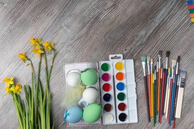 Paskalya yumurtaları, renkli boya ve fırçalar, ahşap arka planda sarı çiçekler. Resim yapmaya başlıyorum. Boşluğu kopyala, seçici odak