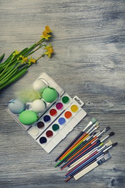 Paskalya yumurtaları, renkli boya ve fırçalar, ahşap arka planda sarı çiçekler. Resim yapmaya başlıyorum. Boşluğu kopyala, seçici odak