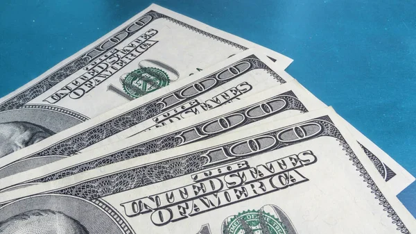 Stack of one hundred dollar bills on blue background, close-up.