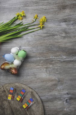 Paskalya yumurtaları, renkli boya ve fırçalar, ahşap arka planda sarı çiçekler. Resim yapmaya başlıyorum. Boşluğu kopyala, seçici odak