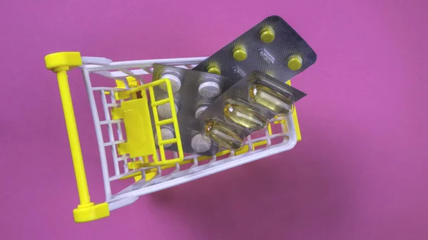 Pills in shopping cart on pink background, health, medicine and pharmacy concept. Pills in shopping cart, copy space