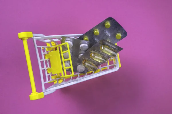 Pills in shopping cart on pink background, health, medicine and pharmacy concept. Pills in shopping cart, copy space