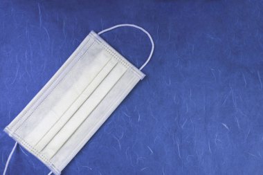 Tıbbi mavi arka planda 3 katmanlı tıbbi maske. Ağız ve burnu kapamak için lastik kulaklıklı maske. Enfeksiyondan korunmak için.