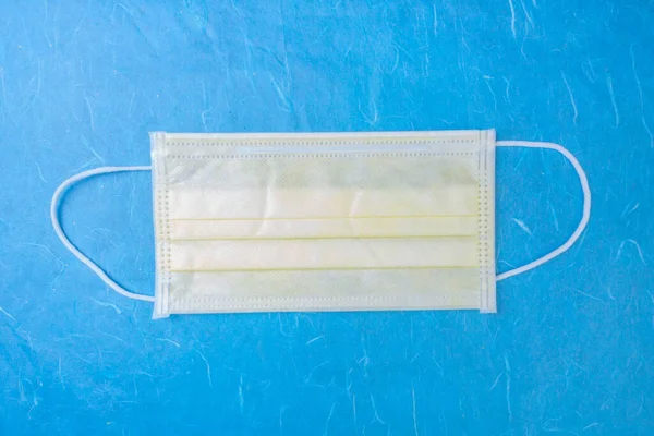 yellow surgical mask with rubber ear straps, medical virus mask on medical blue background, protection concep, top view, copy space