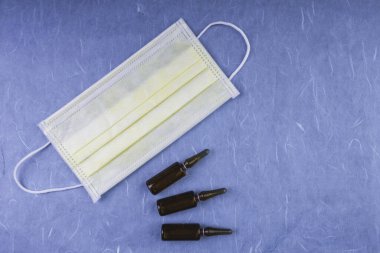 Mavi arka planda tek kullanımlık tıbbi maske. Ağız ve burun için tipik bir üç katmanlı cerrahi maske. Bakteri ve virüslere karşı korunma kavramı, tıbbi ampullerle, boşluğu kopyala