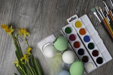 Paskalya yumurtaları, renkli boyalar ve fırça, ahşap arka planda sarı çiçekler. Resim yapmaya başlıyorum. Boşluğu kopyala, seçici odak