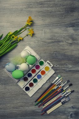 Paskalya yumurtaları, renkli boyalar ve fırça, ahşap arka planda sarı çiçekler. Resim yapmaya başlıyorum. Boşluğu kopyala, seçici odak