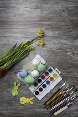 Paskalya yumurtaları, renkli boyalar ve fırça, ahşap arka planda sarı çiçekler. Resim yapmaya başlıyorum. Boşluğu kopyala, seçici odak