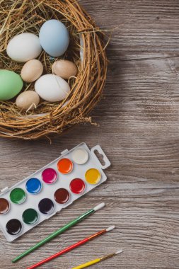 Yuvada paskalya yumurtaları ve ahşap arka planda renkli boya ve fırçalar. Resim yapmaya başlıyorum. Kapat.
