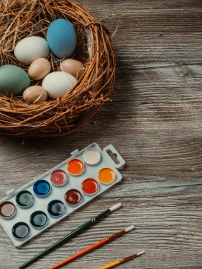 Yuvada paskalya yumurtaları ve ahşap arka planda renkli boya ve fırçalar. Resim yapmaya başlıyorum. Kapat.