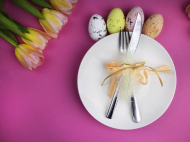 Lüks paskalya sofra takımları bıçak, çatal, pembe yüzey üzerinde renkli laleler. Tatil arkaplanı, tebrik kartı, kapat