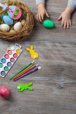 Bebek eli paskalya yumurtasına döner. Ahşap masa boyaları, fırçalar, tavşan, yuva. Yumurta boyamaya hazırlanıyor.