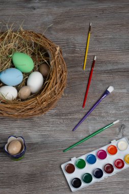 Paskalya tatiline hazırlanıyor, ahşap masa yuvasında renkli yumurtalar, boyalar ve fırçalarla