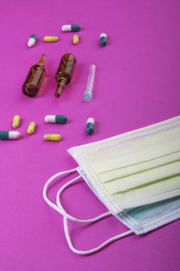 Pembe arka planda koruyucu yüz maskeleri, terapi, virüs gribinin önlenmesi, haplar, ampuller, cam, antibiyotikler, iğne, tıbbi eczane konsepti,