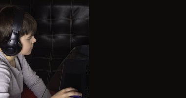 Şık kulaklıklı çocuk dizüstü bilgisayar kullanıyor, defterle vakit geçiriyor ve boş vakitlerin tadını çıkarıyor.