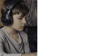 Şık kulaklıklı çocuk dizüstü bilgisayar kullanıyor, defterle vakit geçiriyor ve boş vakitlerin tadını çıkarıyor.