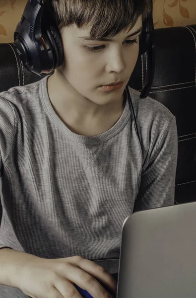 Şık kulaklıklı çocuk dizüstü bilgisayar kullanıyor, defterle vakit geçiriyor ve boş vakitlerin tadını çıkarıyor.