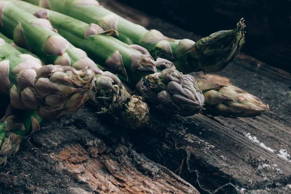 Vitamin, glutathione ve mineraller açısından zengin bir avuç taze yeşil kuşkonmaz. Eski ahşap arka planda.