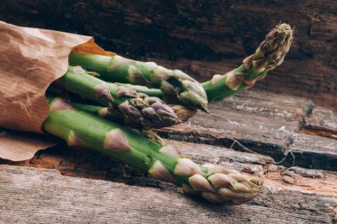 Vitamin, glutathione ve mineraller açısından zengin bir avuç taze yeşil kuşkonmaz. Eski ahşap arka planda.