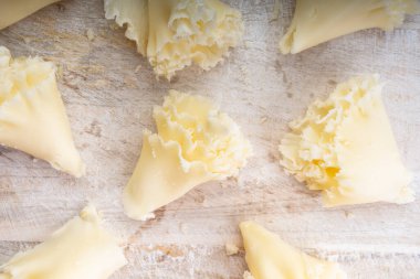 İsviçre peyniri Tete de Moine veya manastır keşişi kafası, özel bir bıçakla kazınmış, beyaz ahşap arka planda kolyeler, yakın plan.