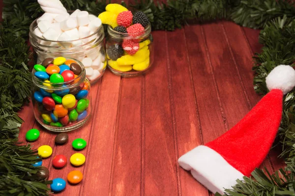 Конфеты разного цвета на деревянном фоне с мишурой и шляпой Санта-Клауса. Копирование пространства — стоковое фото