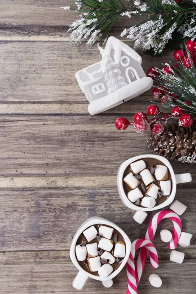 Weihnachtsstillleben - zwei Tassen heiße Schokolade mit Eibisch, Bonbons, Spielzeughaus und Tannenzweig mit Beeren — Stockfoto