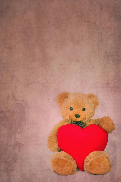 Brown teddy bear with soft heart on textured background