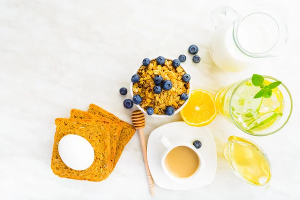 Overhead view on morning dinner table with granola, milk, honey, detox water, coffee, egg and bread