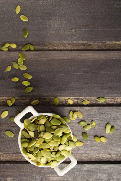 Vue aérienne des graines de citrouille dans un bol blanc sur une table en bois — Photo